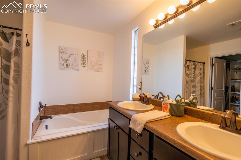 Image 25 of 34: Full bath featuring a shower with shower curtain, double vanity, a bath, an