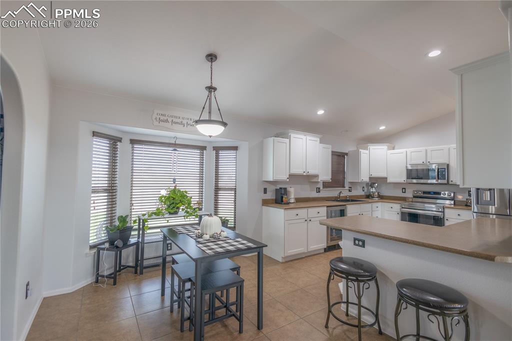 Image 8 of 34: Kitchen with white cabinets, glass insert cabinets, vaulted ceiling, stainl