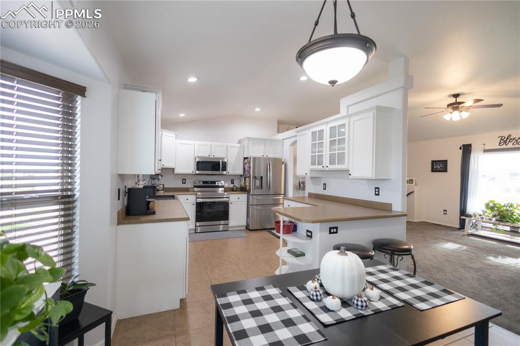 Image 9 of 34: Kitchen with vaulted ceiling, dark countertops, white cabinetry, appliances