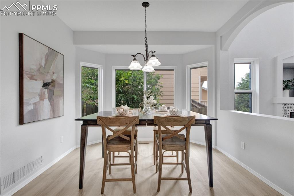 Image 11 of 44: Dining area with light wood-style flooring, arched walkways, and a chandeli
