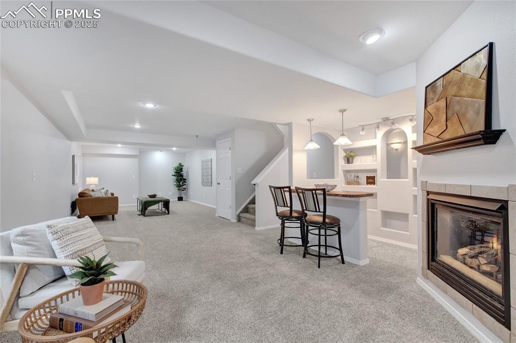 Image 30 of 44: Living room with light carpet, stairway, and a glass covered fireplace