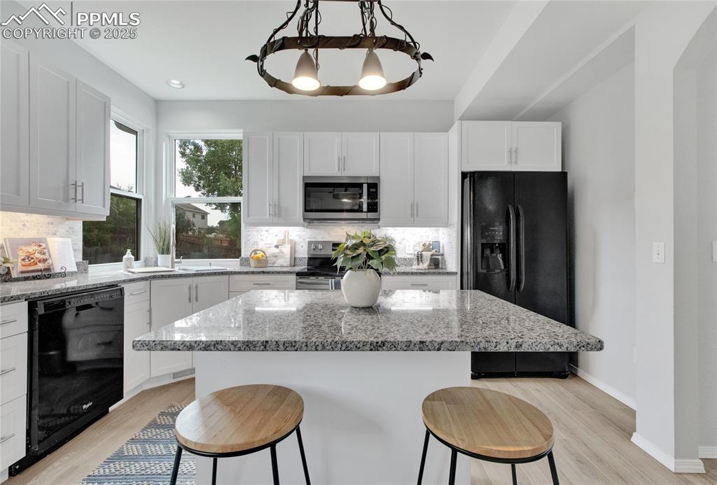 Image 7 of 44: Kitchen with black appliances, a breakfast bar area, and decorative backspl