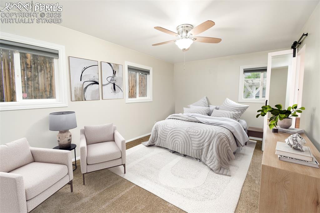 Image 10 of 25: Virtually Staged Bedroom featuring a barn door, ceiling fan, and carpet flo