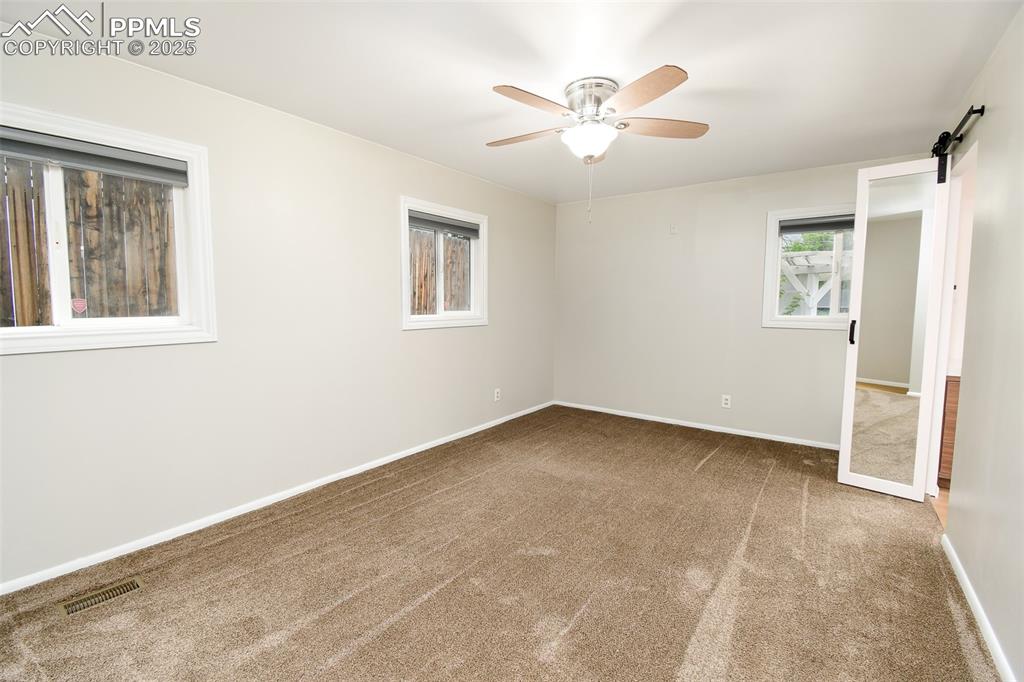 Image 11 of 25: Carpeted empty room with a barn door and ceiling fan