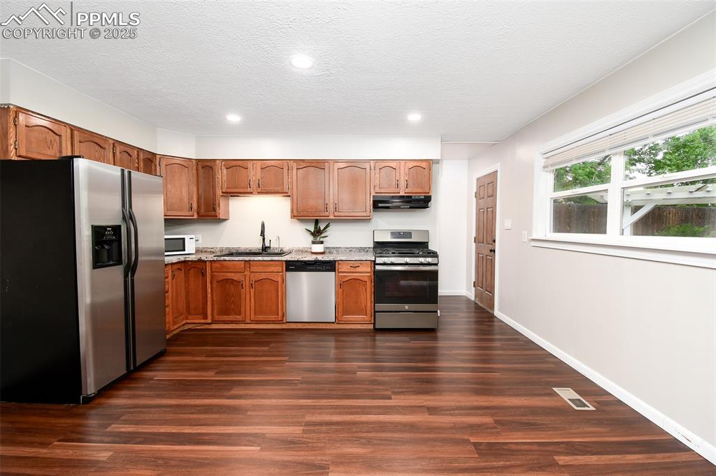 Image 7 of 25: Kitchen with stainless steel appliances, dark wood-style floors, recessed l