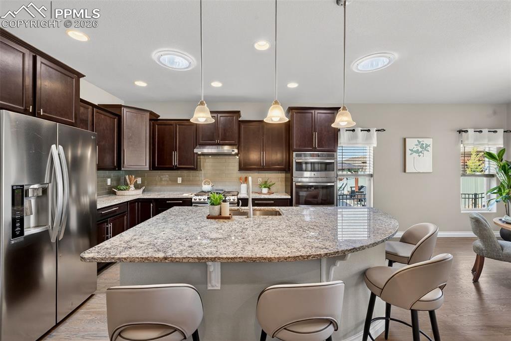 Image 14 of 34: Kitchen with stainless steel appliances, decorative light fixtures, light s