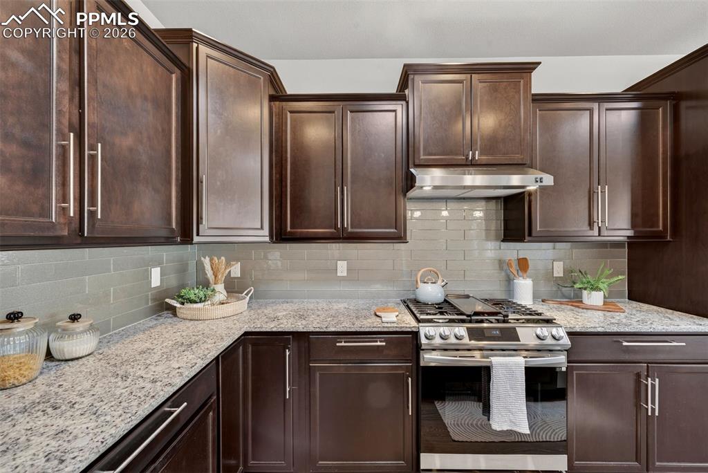 Image 17 of 34: Kitchen with stainless steel gas range, light stone counters, and dark wood