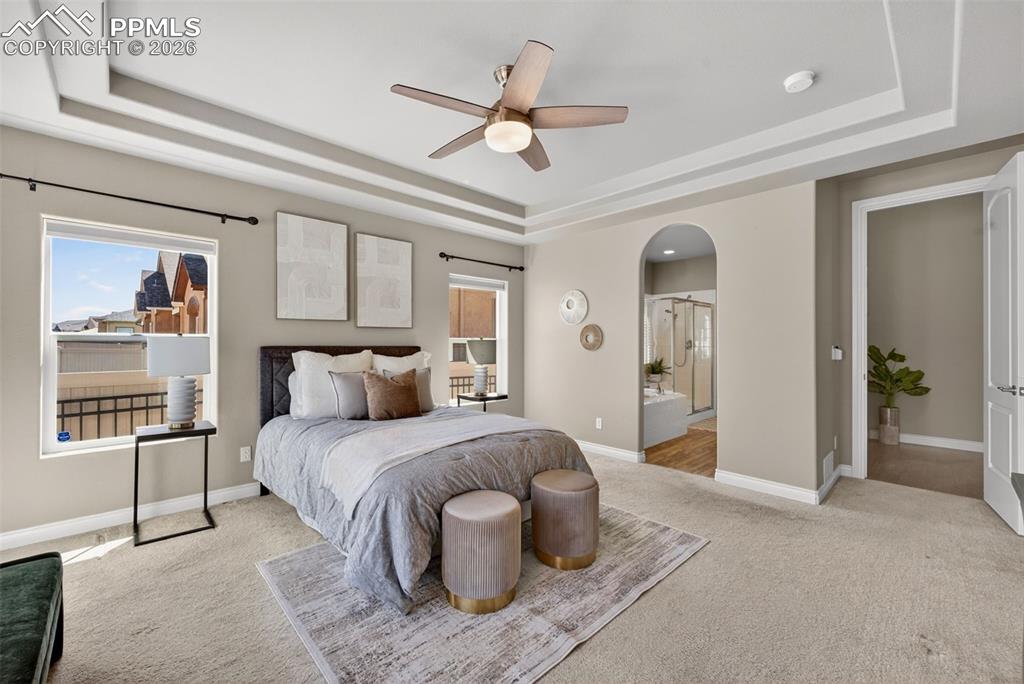 Image 21 of 34: Bedroom with arched walkways, a raised ceiling, light colored carpet, ceili