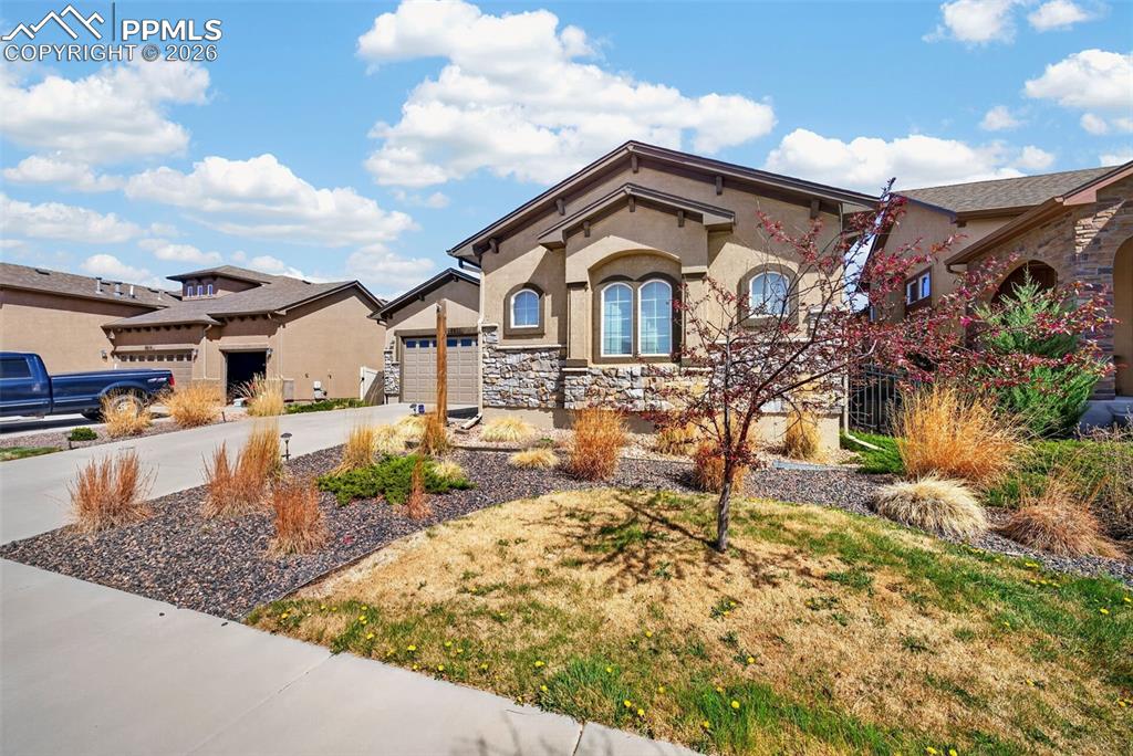 Image 3 of 34: View of front facade featuring stone siding, a garage, driveway, and stucco