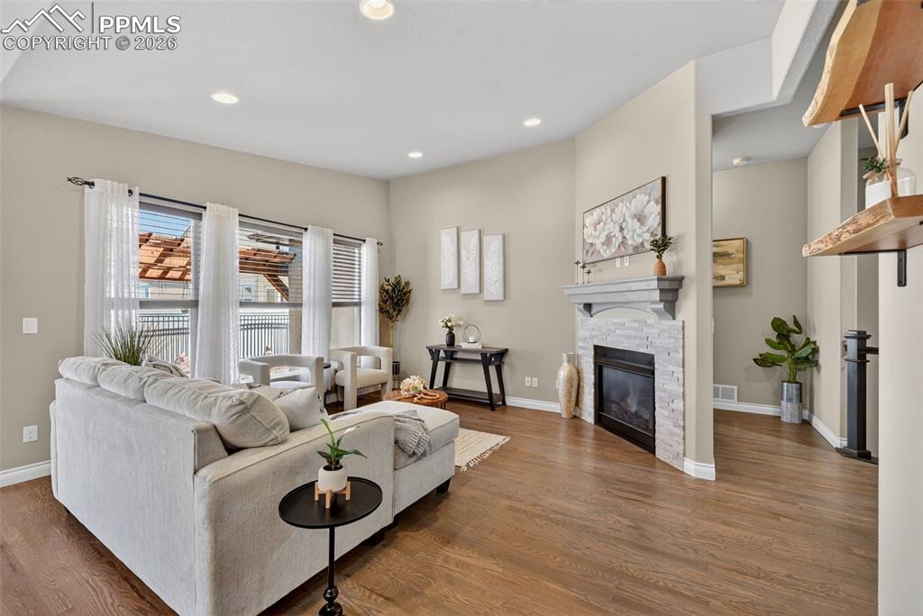 Image 9 of 34: Living room with a stone fireplace, wood finished floors, and recessed ligh