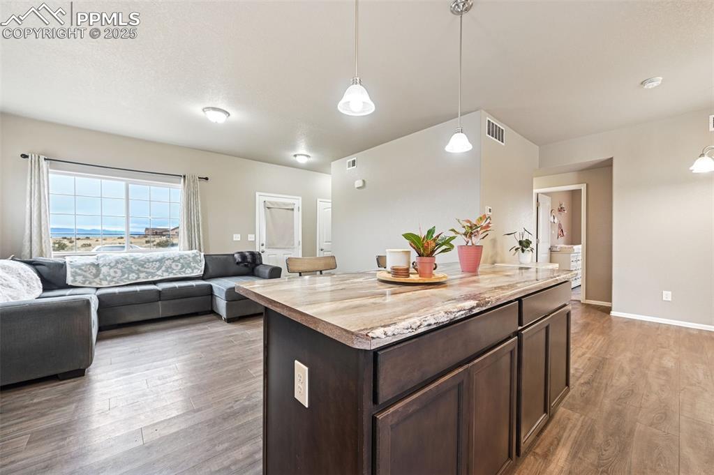 Image 6 of 29: Kitchen featuring dark brown cabinetry, hanging light fixtures, open floor