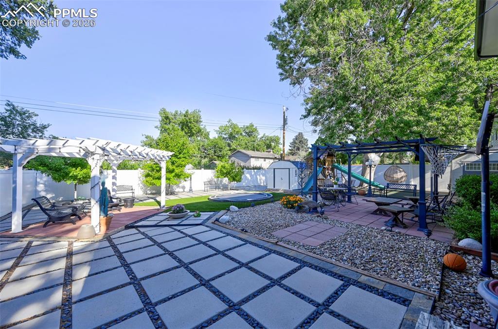 Image 13 of 46: Fenced backyard featuring a pergola, a patio, a storage unit, and a playgro