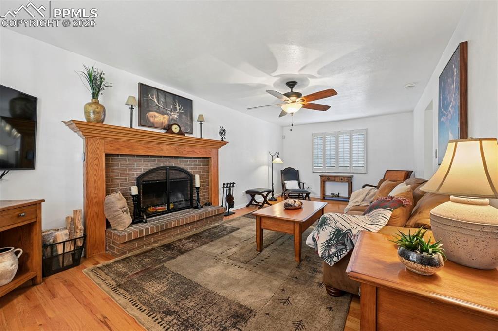 Image 17 of 46: Living room with light wood-style flooring, a fireplace, and a ceiling fan
