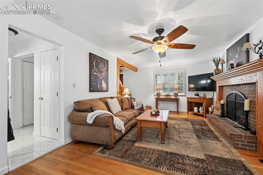 Image 19 of 46: Living area with light wood finished floors, ceiling fan, and a brick firep