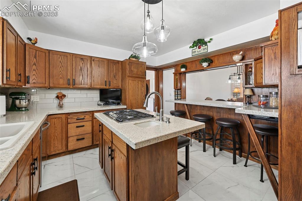 Image 28 of 46: Kitchen with a breakfast bar area, backsplash, wood finish cabinetry, and l