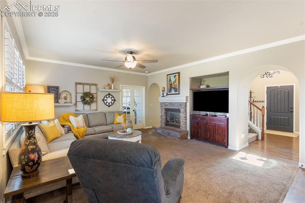Image 13 of 46: Living room featuring crown molding, arched walkways, stairs, a stone firep