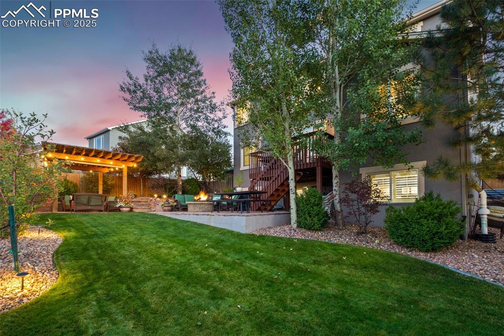 Image 35 of 46: Yard at dusk featuring a lawn, a wooden deck, stairs, and a patio area