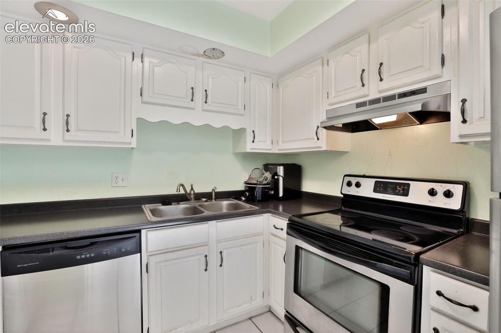 Image 10 of 28: Kitchen featuring white cabinetry, dark countertops, a double basin stainle