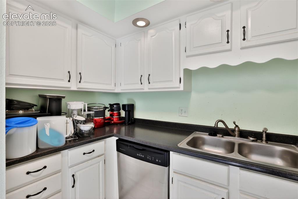 Image 11 of 28: Kitchen featuring white cabinetry with dark hardware, dark countertops, a d