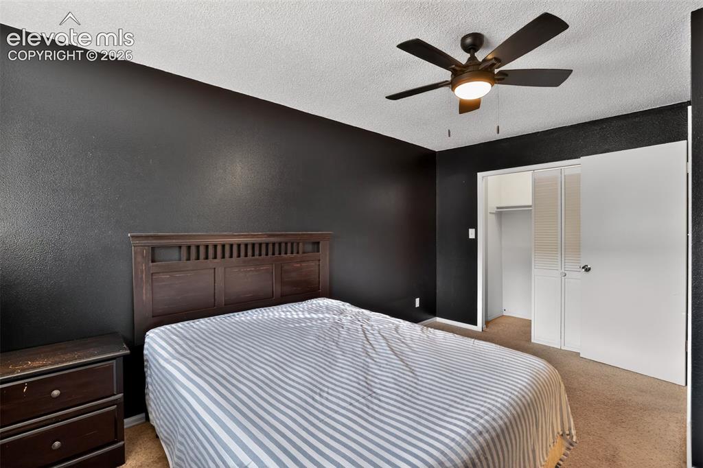 Image 15 of 28: Bedroom featuring dark textured walls, carpet flooring, and a ceiling fan w