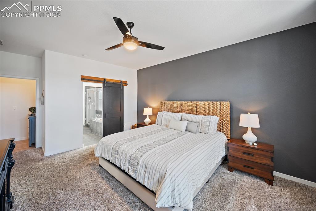 Image 20 of 41: Carpeted bedroom featuring a barn door, ceiling fan, and connected bathroom