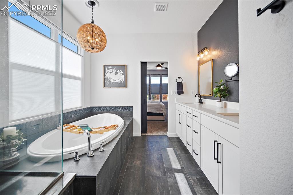 Image 24 of 41: Ensuite bathroom with double vanity, a bath, wood finished floors, and a ch