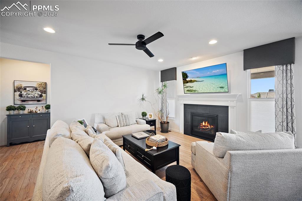 Image 6 of 41: Living room featuring a tiled fireplace, a ceiling fan, light wood finished