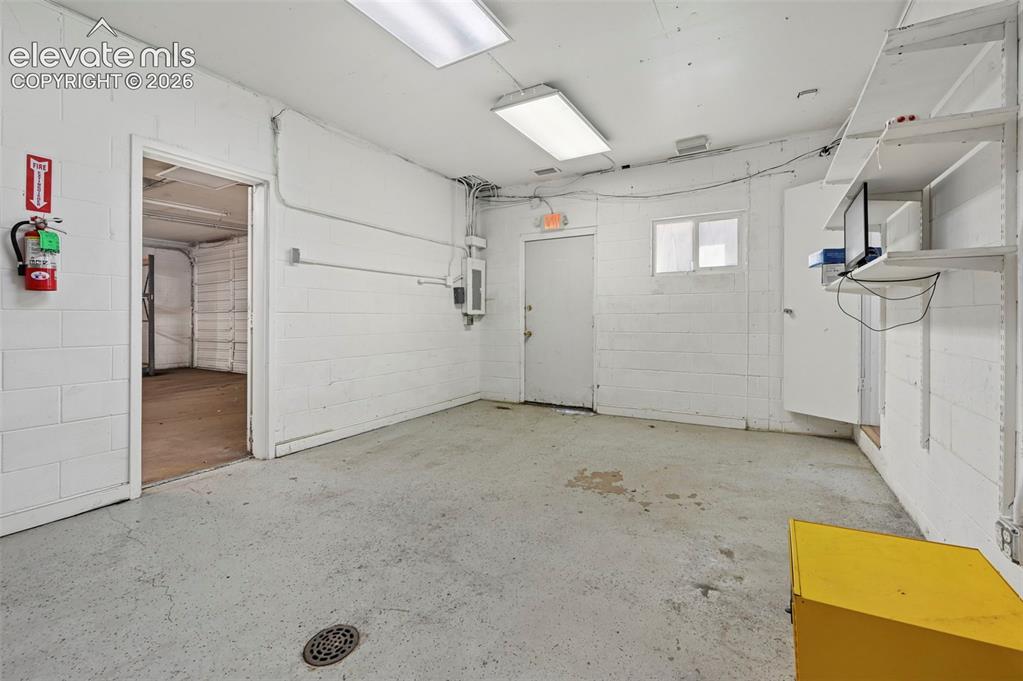 Image 14 of 23: Concrete flooring with a floor drain, white painted block walls, and recess