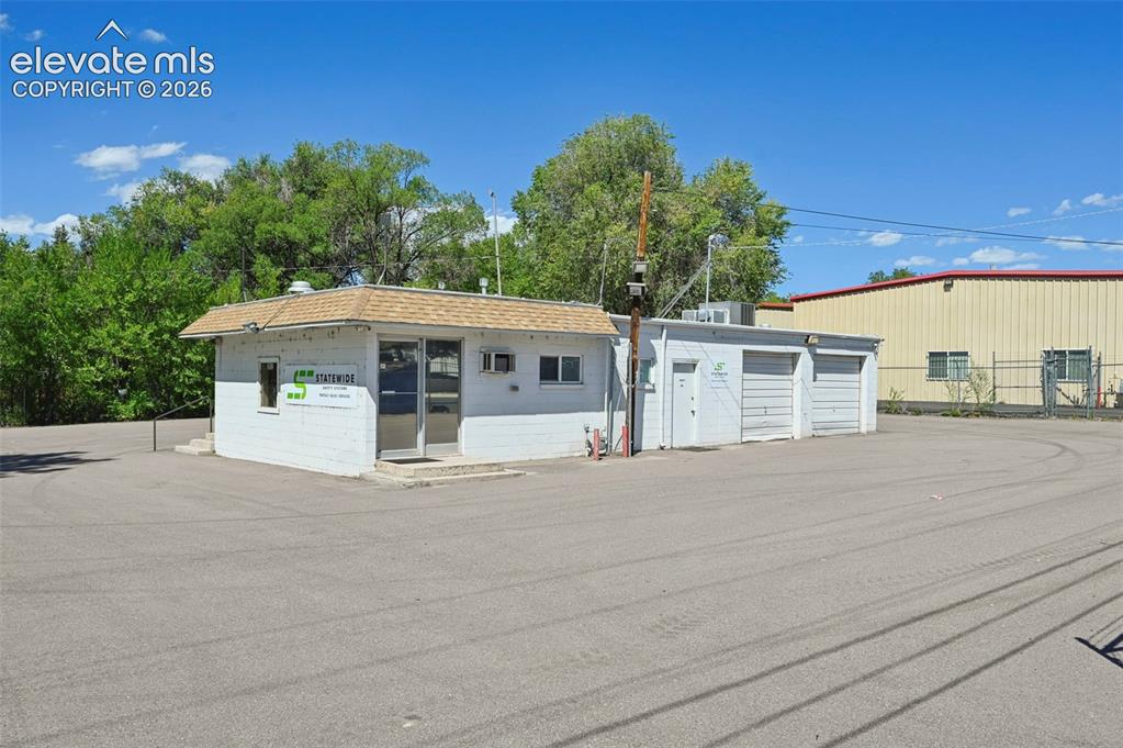 Image 2 of 23: White stucco exterior with a brown shingle roof, multiple garage doors, and