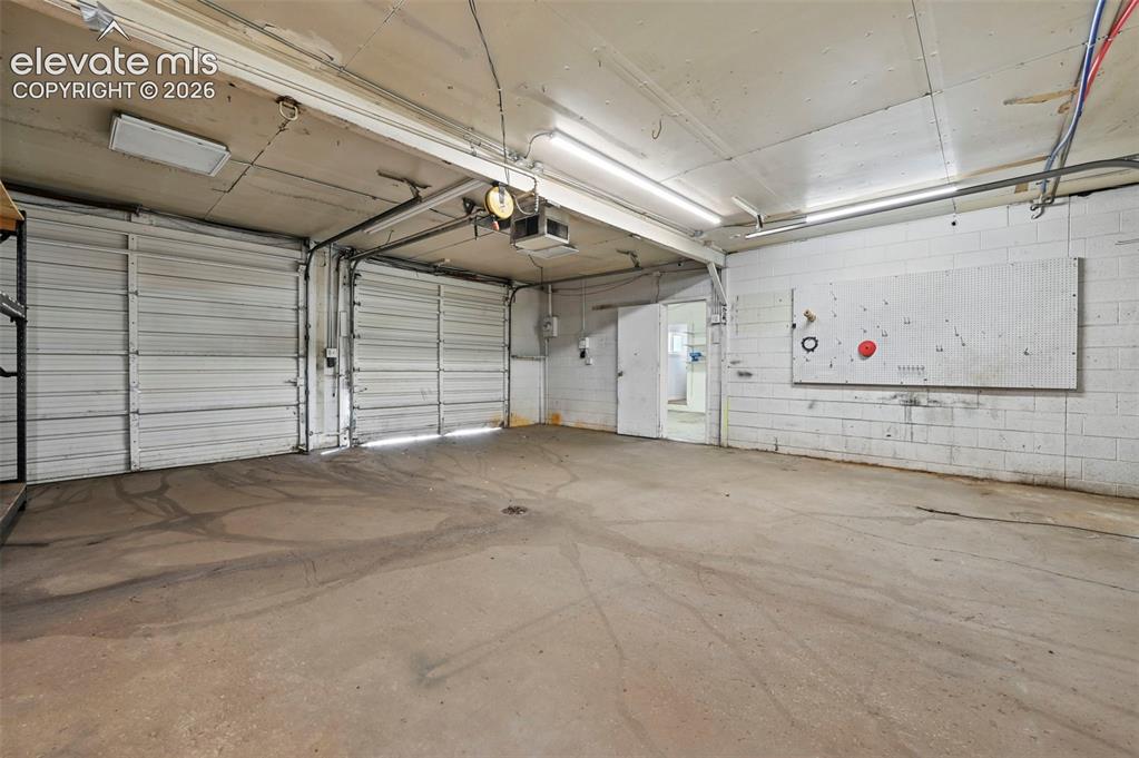 Image 21 of 23: Concrete flooring, dual roll-up doors, and fluorescent lighting