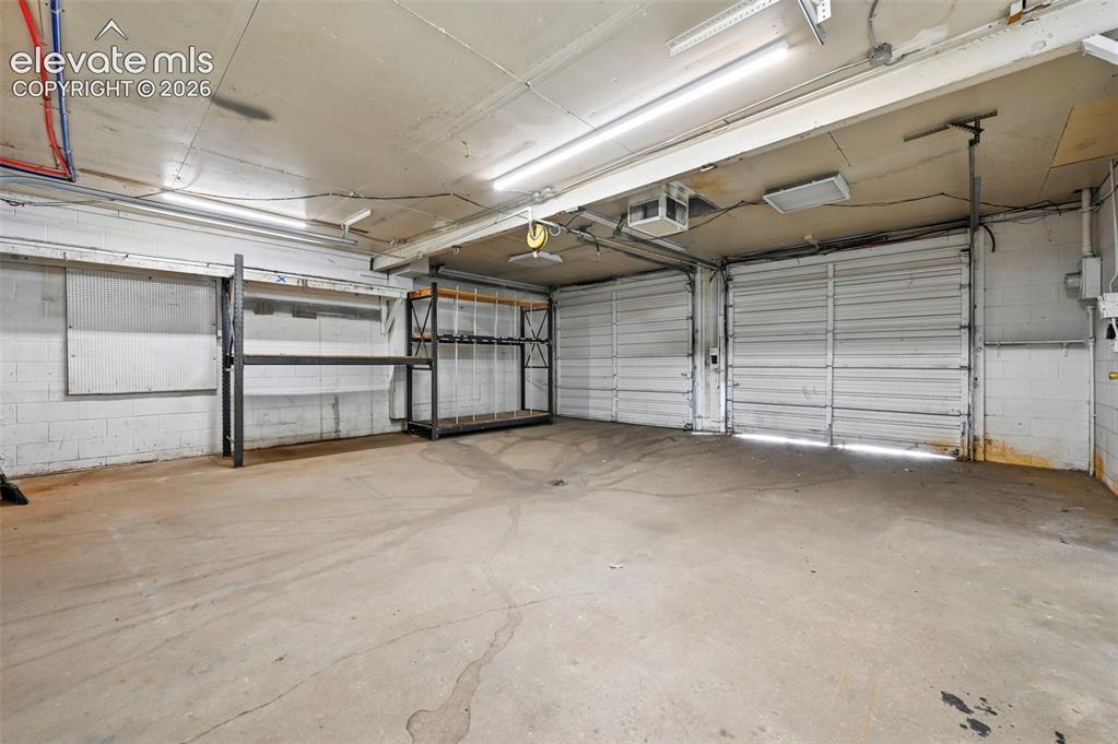 Image 22 of 23: Two overhead garage doors, concrete flooring, exposed ceiling utilities, an