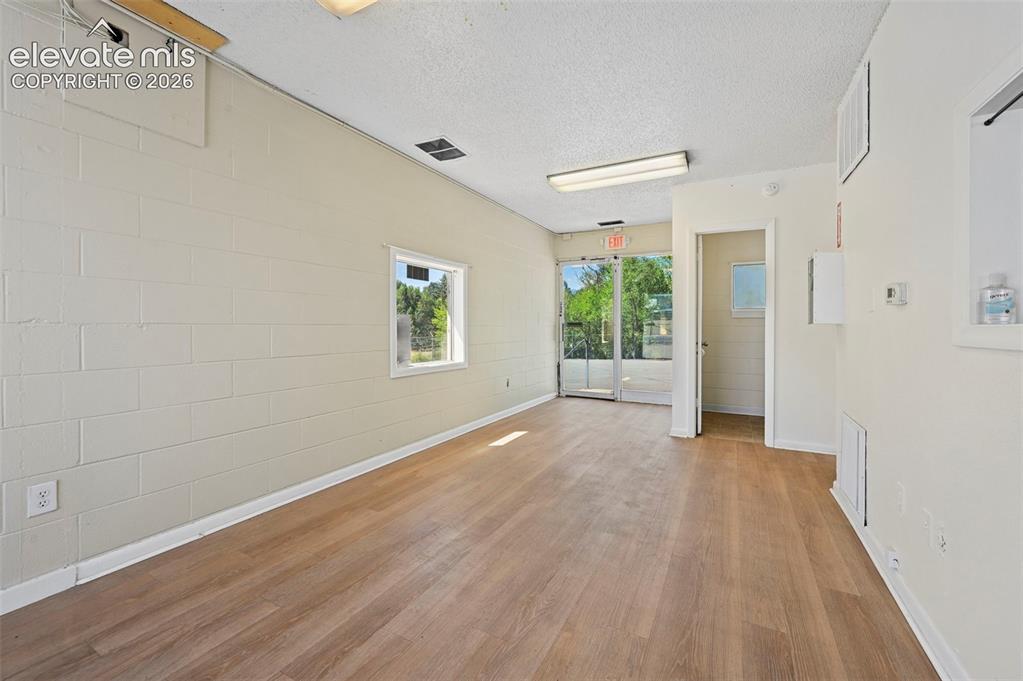 Image 7 of 23: Wood-finish flooring with white baseboards, a single window, and a glass st