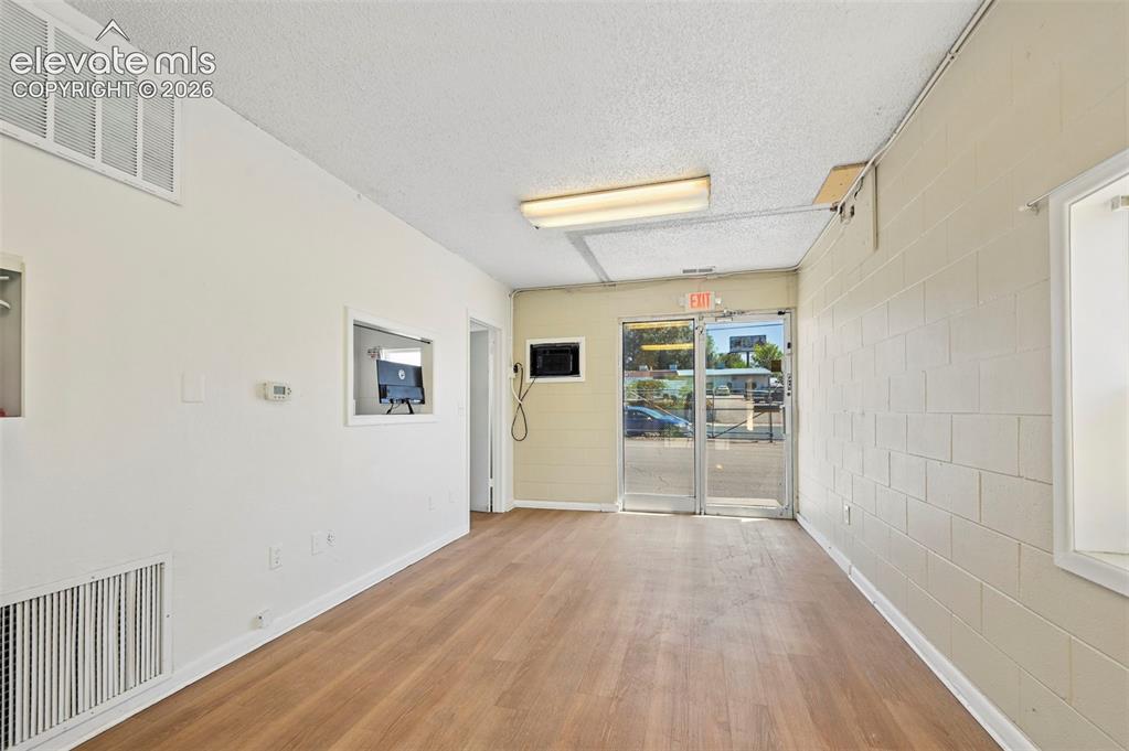 Image 8 of 23: Wood-finish flooring, white painted walls, exposed block wall, drop ceiling