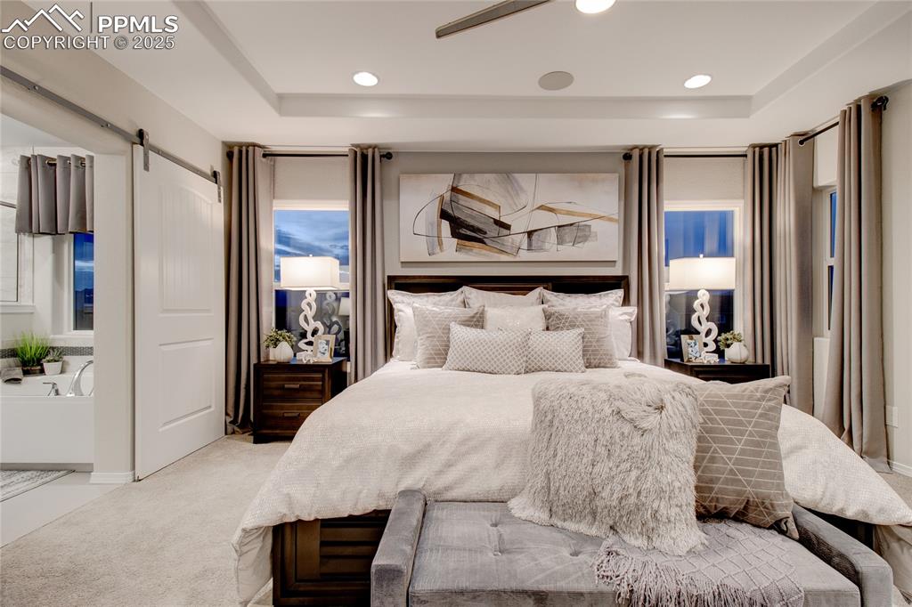 Image 19 of 28: Bedroom featuring a barn door, light colored carpet, ceiling fan, recessed 