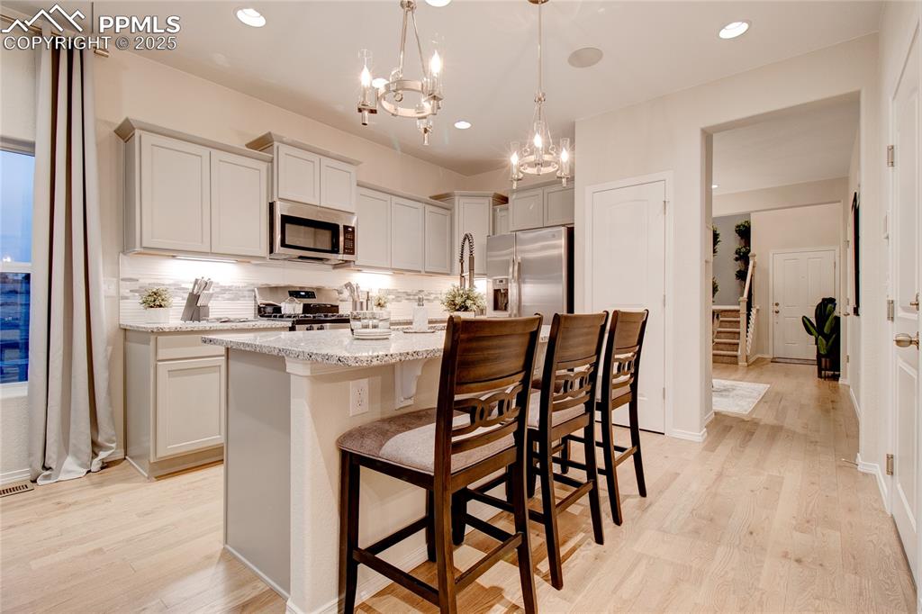 Image 9 of 28: Kitchen featuring a kitchen bar, an island with sink, decorative backsplash