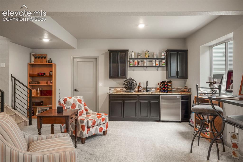 Image 22 of 31: Lower-level recreation space featuring a built-in wet bar with dark cabinet