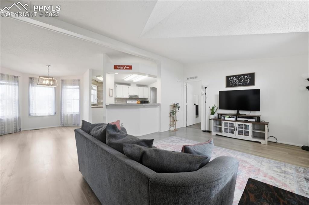 Image 12 of 45: Living room with vaulted ceiling, light wood finished floors, and a texture