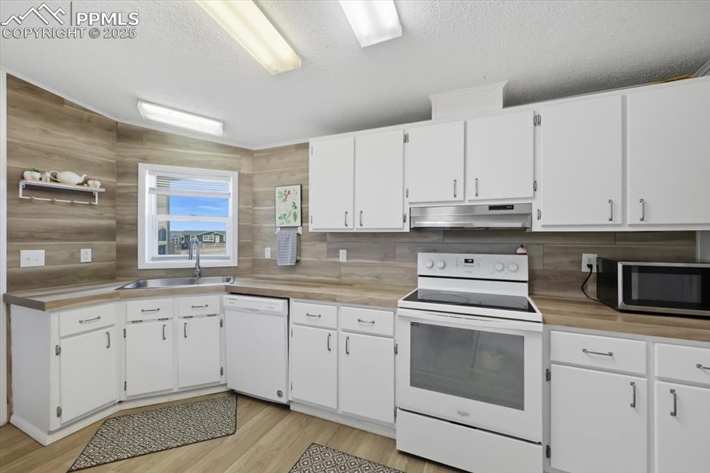 Image 20 of 45: Kitchen with white cabinetry, white appliances, light countertops, a textur