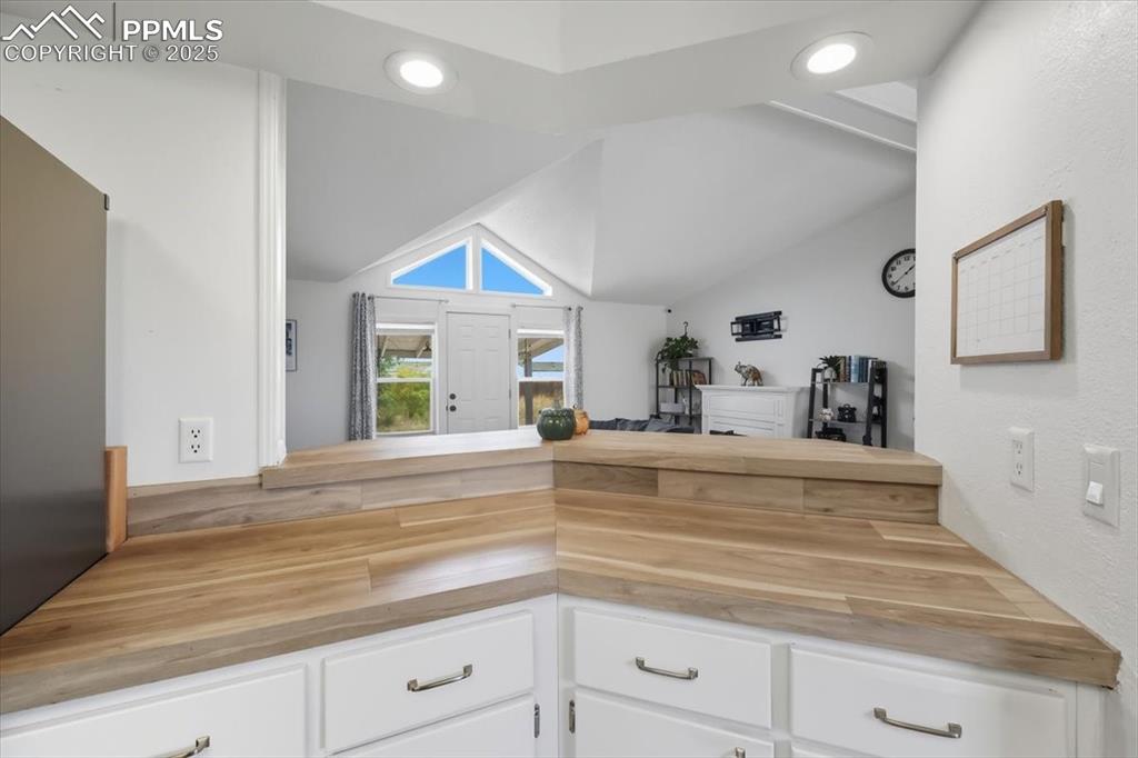 Image 21 of 45: Kitchen featuring white cabinets, butcher block countertops, lofted ceiling