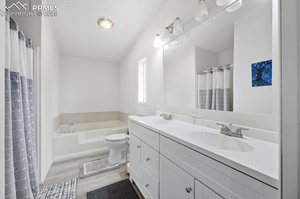 Image 25 of 45: Bathroom featuring double vanity, a bath, light wood finished floors, and a