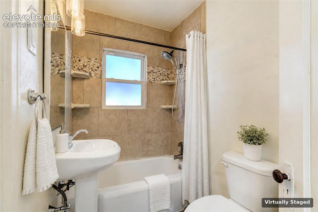 Image 2 of 50: Bathroom featuring a pedestal sink, a bathtub with a shower head, tile wall