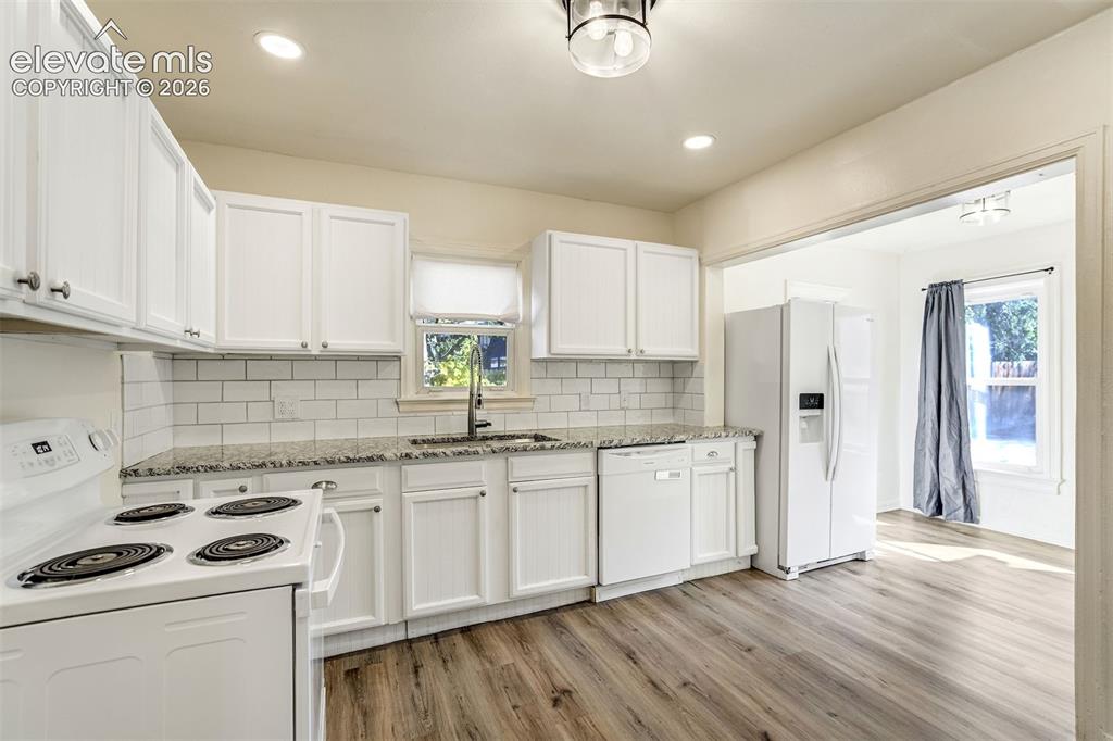 Image 20 of 50: Kitchen featuring white cabinetry, stone-surface countertops, subway tile b