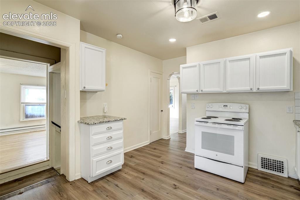 Image 21 of 50: Kitchen featuring white cabinetry, stone-surface countertops, wood-finish f