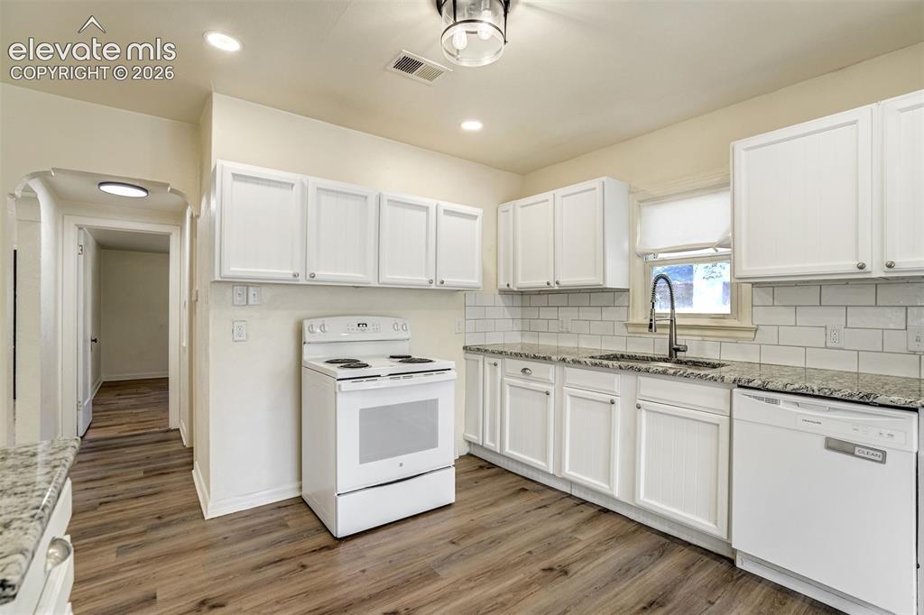 Image 22 of 50: Kitchen featuring white cabinetry, stone-finish countertops, subway tile ba