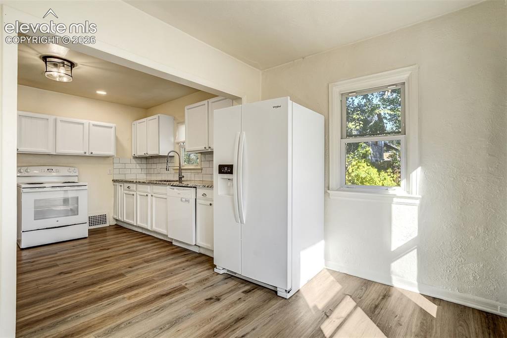 Image 28 of 50: Kitchen featuring white cabinetry, wood-finish flooring, subway tile backsp