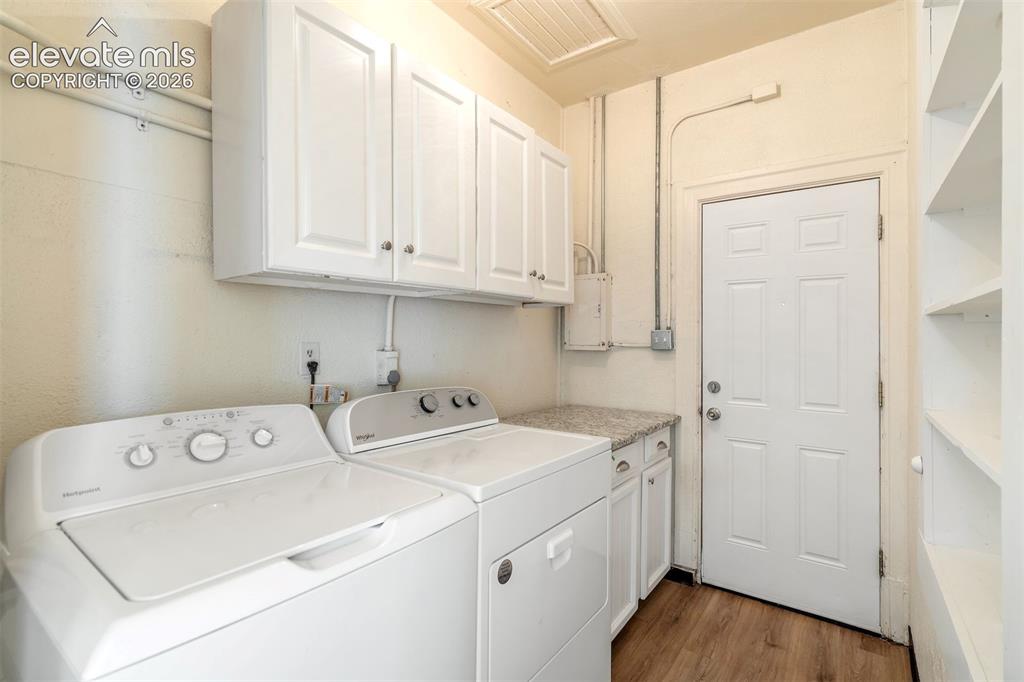 Image 33 of 50: Laundry area featuring wood-finish flooring, white cabinetry, a stone-compo