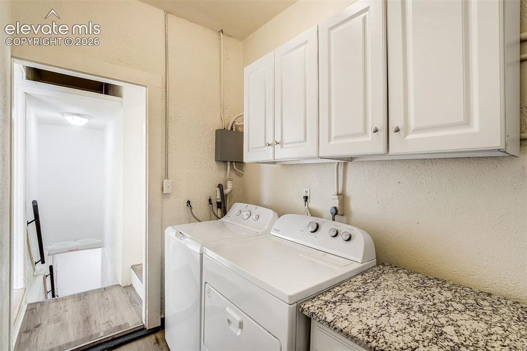 Image 34 of 50: Laundry area featuring white shaker-style wall cabinets, speckled stone-fin