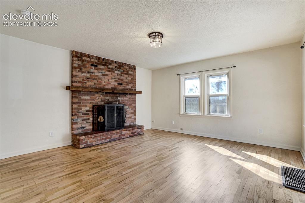 Image 7 of 50: Full-height brick fireplace with a wood mantel, wood-finish flooring, and t