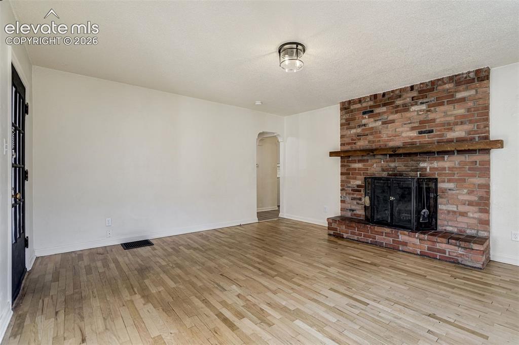 Image 8 of 50: Living area featuring wood-finish flooring, a floor-to-ceiling brick firepl