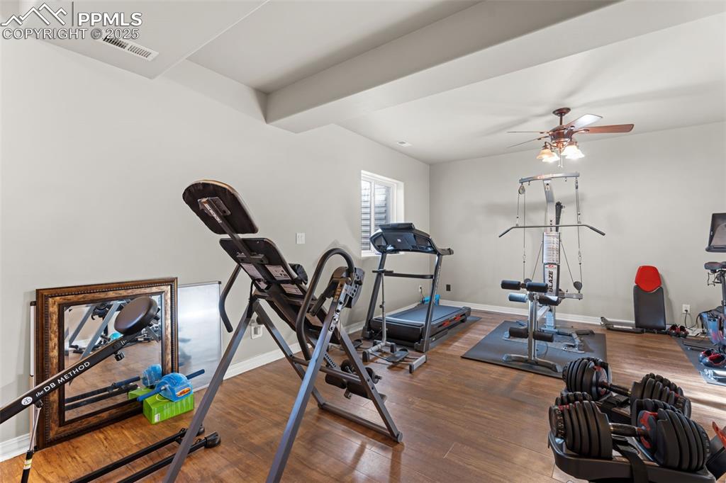 Image 29 of 41: Exercise area featuring dark wood finished floors, ceiling fan, and beam ce